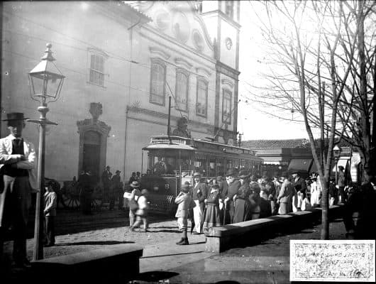 Foto (Junho/1900): Acervo Fundação Energia e Saneamento 1. Parada de bonde elétrico e multidão, no Largo São Bento, mostrando à esquerda o Mosteiro e ao fundo o casario da Rua Florêncio de Abreu.