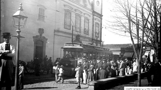 Foto (Junho/1900): Acervo Fundação Energia e Saneamento 1. Parada de bonde elétrico e multidão, no Largo São Bento, mostrando à esquerda o Mosteiro e ao fundo o casario da Rua Florêncio de Abreu.